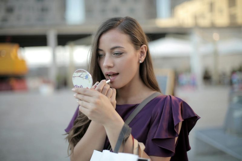 shallow focus photo of woman applying lipstick