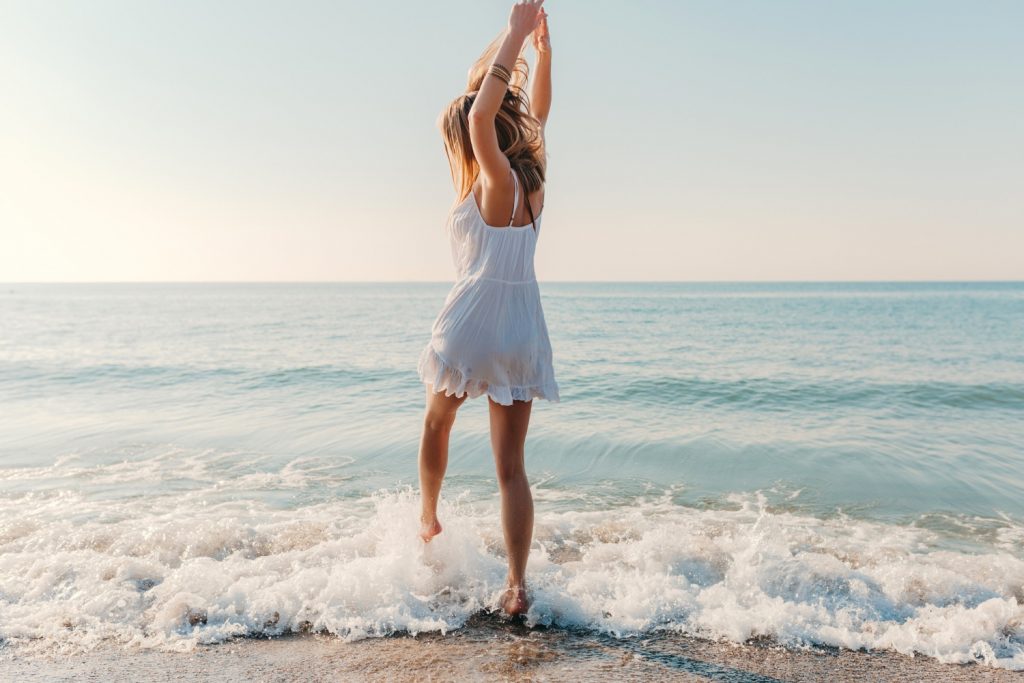 Mujer con vestido blanco bailando con las olas a orillas del mar