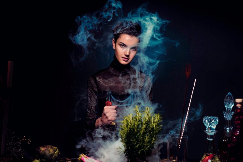 alluring young woman preparing potion against black background